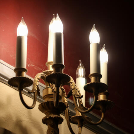 A photograph of a golden candelabra against a white and red wall which fades to black shadows.